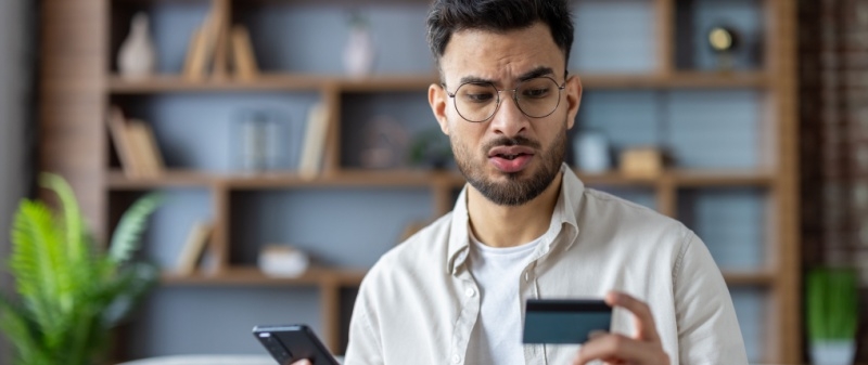 Decorative image - Concerned man looking at credit card and phone