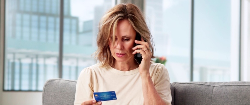 Decorative image - Woman on mobile phone referring to credit card in her hand