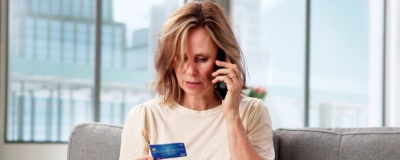 Decorative image - Woman on mobile phone referring to credit card in her hand